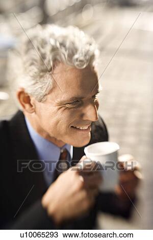 Stock Image - Selective focus close up of prime adult Caucasian man in suit drinking coffee and smiling.. Fotosearch
