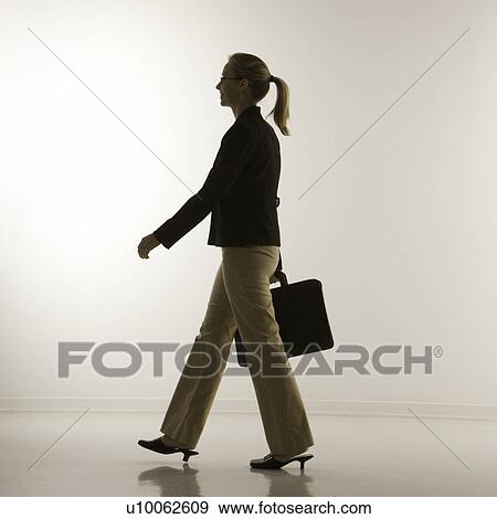 Stock Photo - Silhouette of mid-adult Caucasian businesswoman walking and carrying briefcase.. Fotosearch
