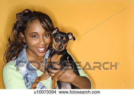 African American young adult female holding Miniature Pinscher dog. View Large Photo Image Picture - African American young adult female holding Miniature Pinscher dog.. Fotosearch