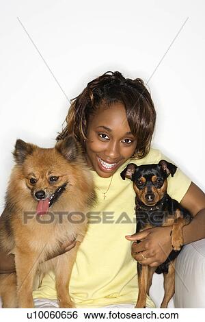 Stock Photograph - African American young adult female holding brown Pomeranian and Miniature Pinscher dogs.. Fotosearch