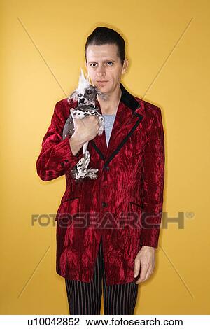 Stock Image - Caucasian mid-adult male wearing velvet holding Chinese Crested dog.. Fotosearch