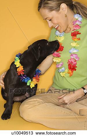 Stock Image - Caucasian prime adult female sitting with black puppy wearing leis.. Fotosearch