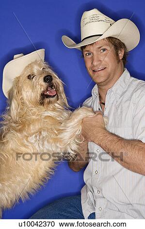 Stock Image - Fluffy brown dog and male Caucasian young adult wearing cowboy hats.. Fotosearch