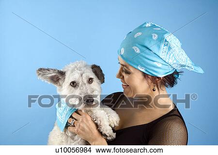 Picture - Hispanic mid-adult woman holding small white dog wearing matching bandanas.. Fotosearch