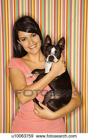 Stock Photo - Young adult female Caucasian holding Boston Terrier dog on striped background.. Fotosearch