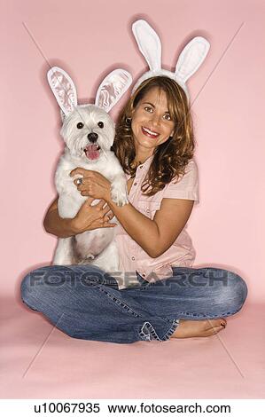Stock Photography - Caucasian prime adult female and white terrier dog wearing rabbit ears.. Fotosearch