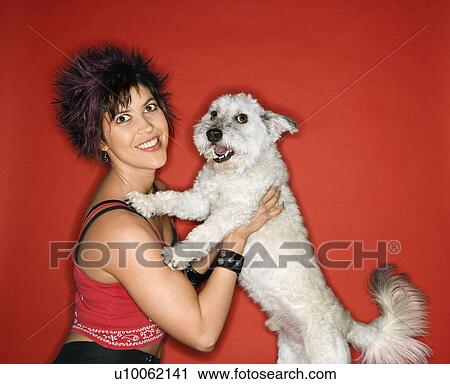 Stock Image - Hispanic young adult female holding small white dog.. Fotosearch