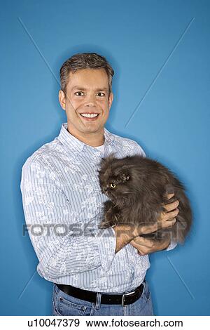 Stock Photo - Mid-adult Caucasian man standing holding Persian cat.. Fotosearch