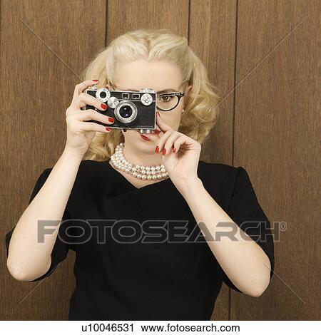 Stock Image - Mid-adult Caucasian female in vintage outfit holding a vintage film camera up to her face.. Fotosearch