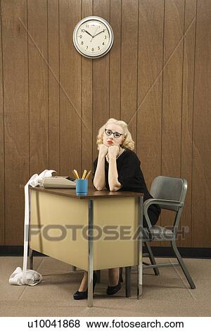 Stock Photo - Mid-adult Caucasian female in vintage outfit sitting at desk with chin on her fists.. Fotosearch