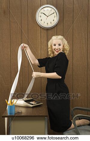 Stock Photograph - Mid-adult Caucasian female in vintage outfit holding a printout from calculator in her office.. Fotosearch