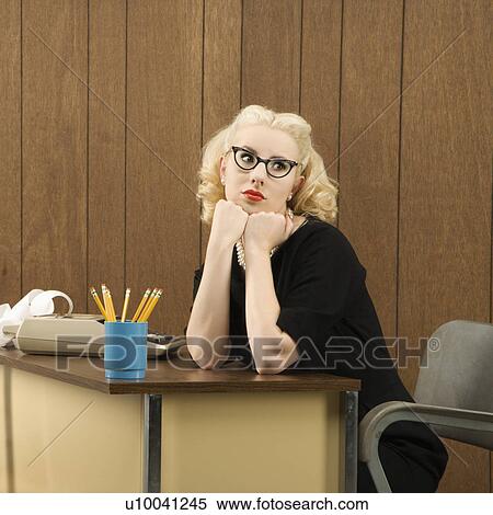 Stock Photography - Mid-adult Caucasian female in vintage outfit sitting at desk with chin on her fists.. Fotosearch