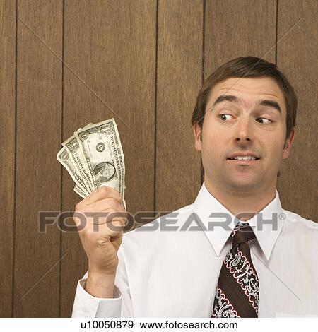 Mid-adult Caucasian male holding dollar bills and looking towards them. View Large Photo Image Stock Photo - Mid-adult Caucasian male holding dollar bills and looking towards them.. Fotosearch