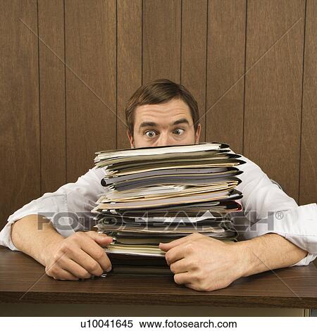 Stock Photography - Mid-adult Caucasian male peeking over big stack of paperwork.. Fotosearch