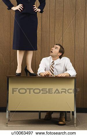 Mid-adult Caucasian male sitting at desk looking up to Caucasian female standing on desk. View Large Photo Image Stock Photo - Mid-adult Caucasian male sitting at desk looking up to Caucasian female standing on desk.. Fotosearch