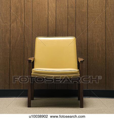 Stock Image - Retro chair against wood paneling in office.. Fotosearch