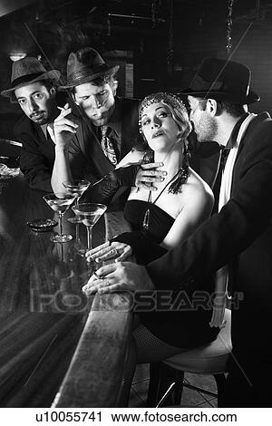 Stock Image - Caucasian prime adult retro female sitting at bar surrounded by suitors.. Fotosearch