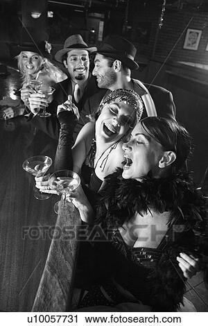 Stock Image - Caucasian prime adult retro females and males sitting at bar.. Fotosearch