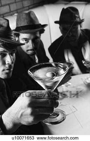Stock Image - Three Caucasian prime adult males in retro suits sitting at table with martini.. Fotosearch