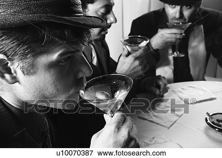 Stock Photo - Three Caucasian prime adult males in retro suits sitting at table drinking cocktails.. Fotosearch
