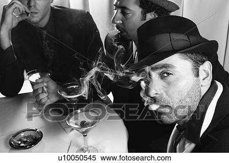 Stock Photography - Three Caucasian prime adult males in retro suits sitting at table drinking cocktails.. Fotosearch