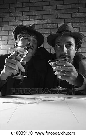 Stock Image - Two Caucasian prime adult males in retro suits sitting at table with martinis.. Fotosearch