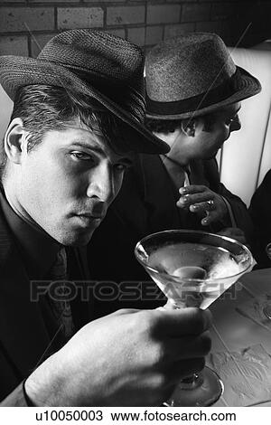 Stock Image - Two Caucasian prime adult males in retro suits sitting at table with cocktails.. Fotosearch