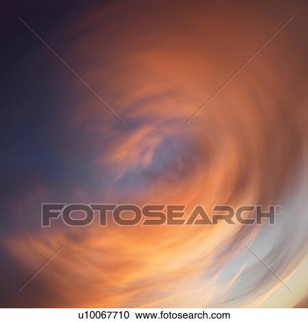 Stock Image - Spiral orange clouds in sky with sunset.. Fotosearch