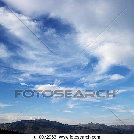 Stock Image - Cloud formations against blue sky with mountain range off in the distance.. Fotosearch