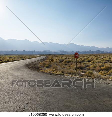 Stock Image - Road with stop sign in barren landscape with mountain in distance.. Fotosearch