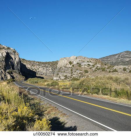 Strip of highway cutting through montain range under clear blue sky. View Large Photo Image Picture - Strip of highway cutting through montain range under clear blue sky.. Fotosearch
