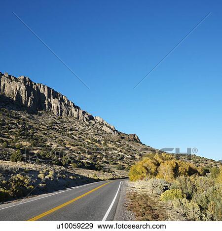 Strip of highway cutting through montain range under clear blue sky. View Large Photo Image Stock Photo - Strip of highway cutting through montain range under clear blue sky.. Fotosearch