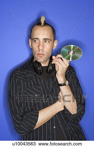 Caucasian man with mohawk with headphones holding cd standing against blue background. View Large Photo Image Stock Image - Caucasian man with mohawk with headphones holding cd standing against blue background.. Fotosearch