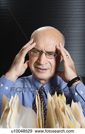 Stock Photo - Caucasian middle-aged businessman looking at files with hands on head and grimacing.. Fotosearch