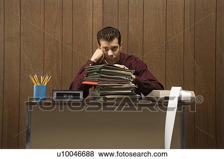 Caucasion mid-adult retro businessman with bored expression sitting at desk piled high with folders. View Large Photo Image Stock Photo - Caucasion mid-adult retro businessman with bored expression sitting at desk piled high with folders.. Fotosearch
