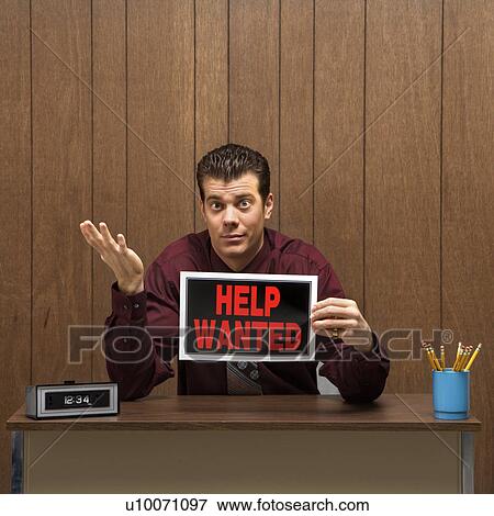 Stock Photo - Caucasion mid-adult retro businessman sitting at desk holding help wanted sign with pleading expression.. Fotosearch