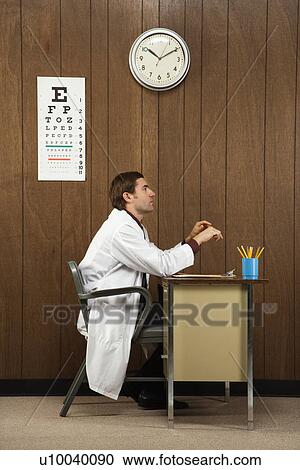 Side view of mid-adult Caucasian male doctor sitting at desk. View Large Photo Image Stock Image - Side view of mid-adult Caucasian male doctor sitting at desk. . Fotosearch
