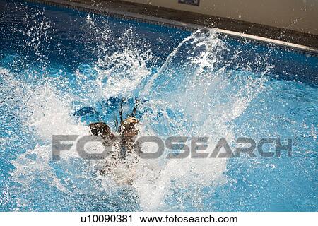 Stock Image - Young couple jumping in pool. Fotosearch