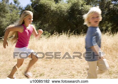 Stock Image - Young girl and young boy running in park. Fotosearch