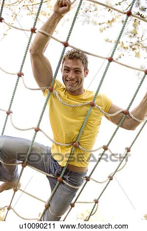 Stock Image - Man on rope climbing frame. Fotosearch