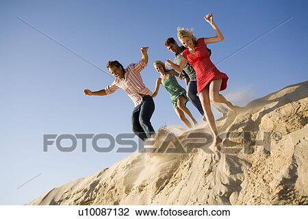 Two couples on beach jumping off sand dune View Large Photo Image Stock Image - Two couples on beach jumping off sand dune. Fotosearch