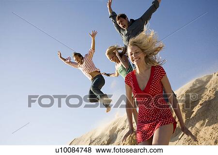 Two couples on beach jumping off sand dune View Large Photo Image Stock Photo - Two couples on beach jumping off sand dune. Fotosearch