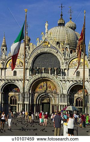 St Marks Basilica in afternoon sunlight. Crowds of tourists, pigeons in the foreground. Italian flag and winged lion flags on poles. View Large Photo Image Stock Photo - St Marks Basilica in afternoon sunlight. Crowds of tourists, pigeons in the foreground. Italian flag and winged lion flags on poles.. Fotosearch