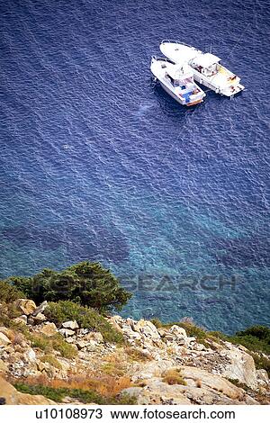 Stock Image - Rocky shoreline and blue green water of coastline with boats Elba Italy. Fotosearch
