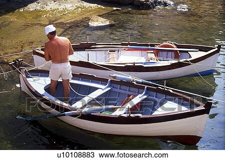 Stock Image - Small rowboats moored in rocky inlet Elba Italy with fisherman. Fotosearch