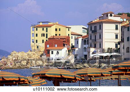 Stock Image - Beachside housing, red yellow white with umbrellas in foreground Elba Italy. Fotosearch