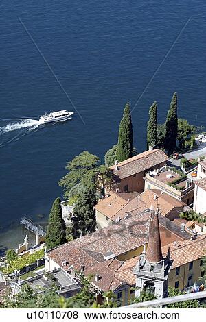 Stock Photo - Boat in water offshore Lago di Como with red tiled rooftops. Fotosearch