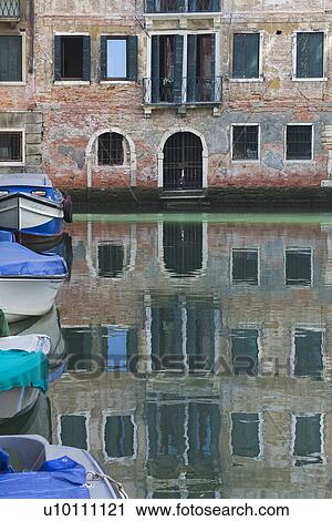 Stock Image - Building reflected in quite canal - boats moored at side. Fotosearch