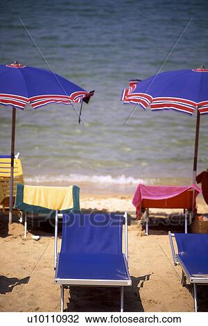 Stock Image - Umbrella and beach chairs on sand at waters edge Italy. Fotosearch