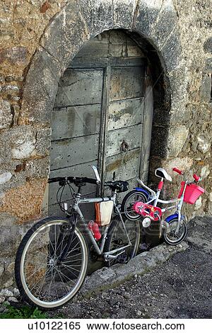 Stock Photography - Adult and childs bikes chained to old arched wooden door. Fotosearch